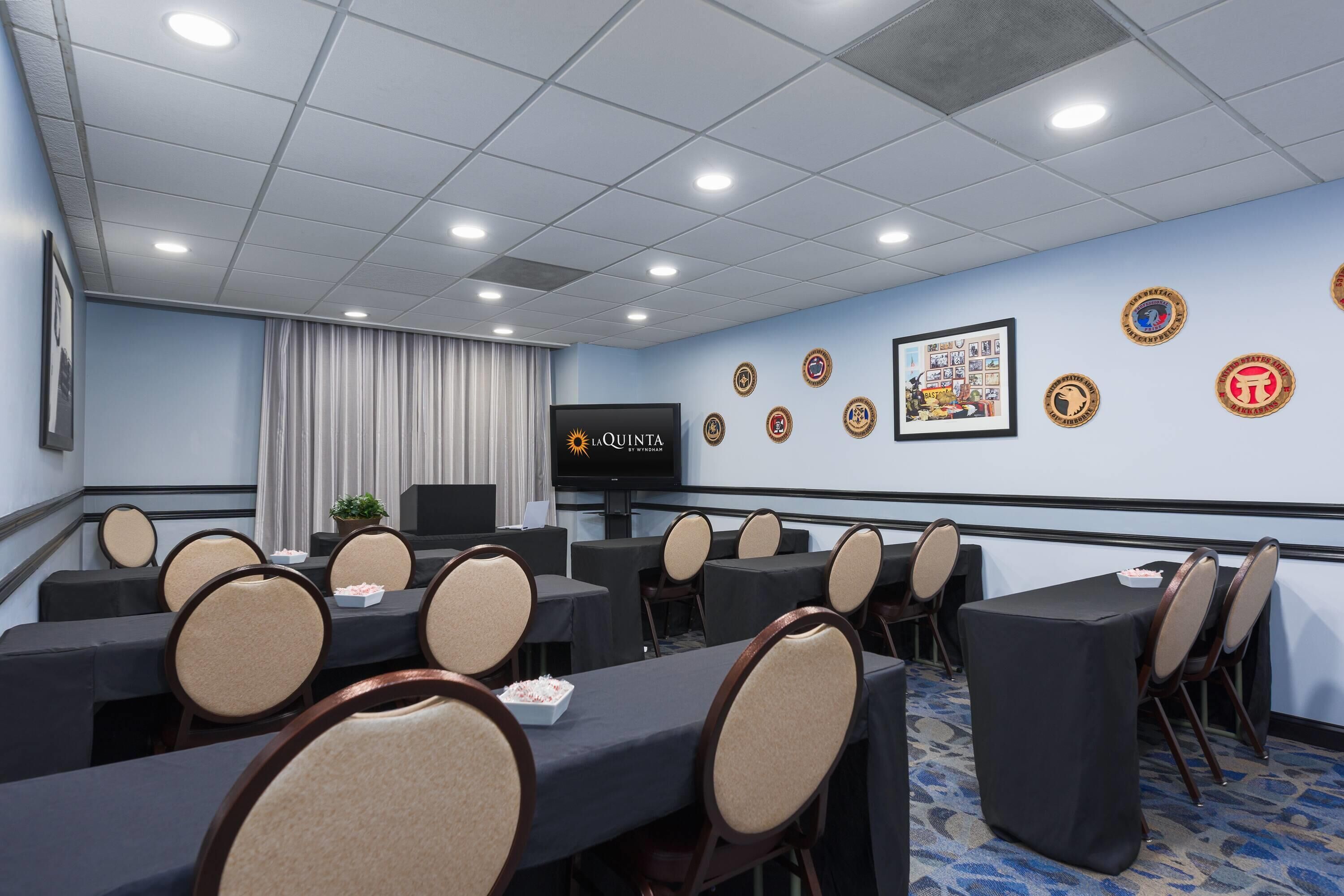 Une salle de conférence équipée de tables, de chaises, d’un écran de projection et de certificats encadrés accrochés au mur.