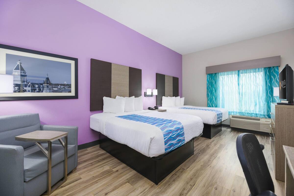 Habitación de hotel con dos camas, un escritorio, una silla, un televisor y una ventana con cortinas.