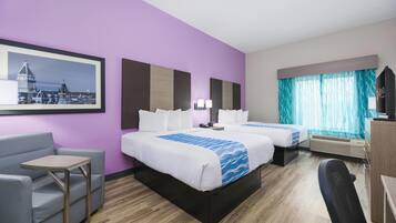 A hotel room with two beds, a desk, a chair, a TV, and a window with curtains.