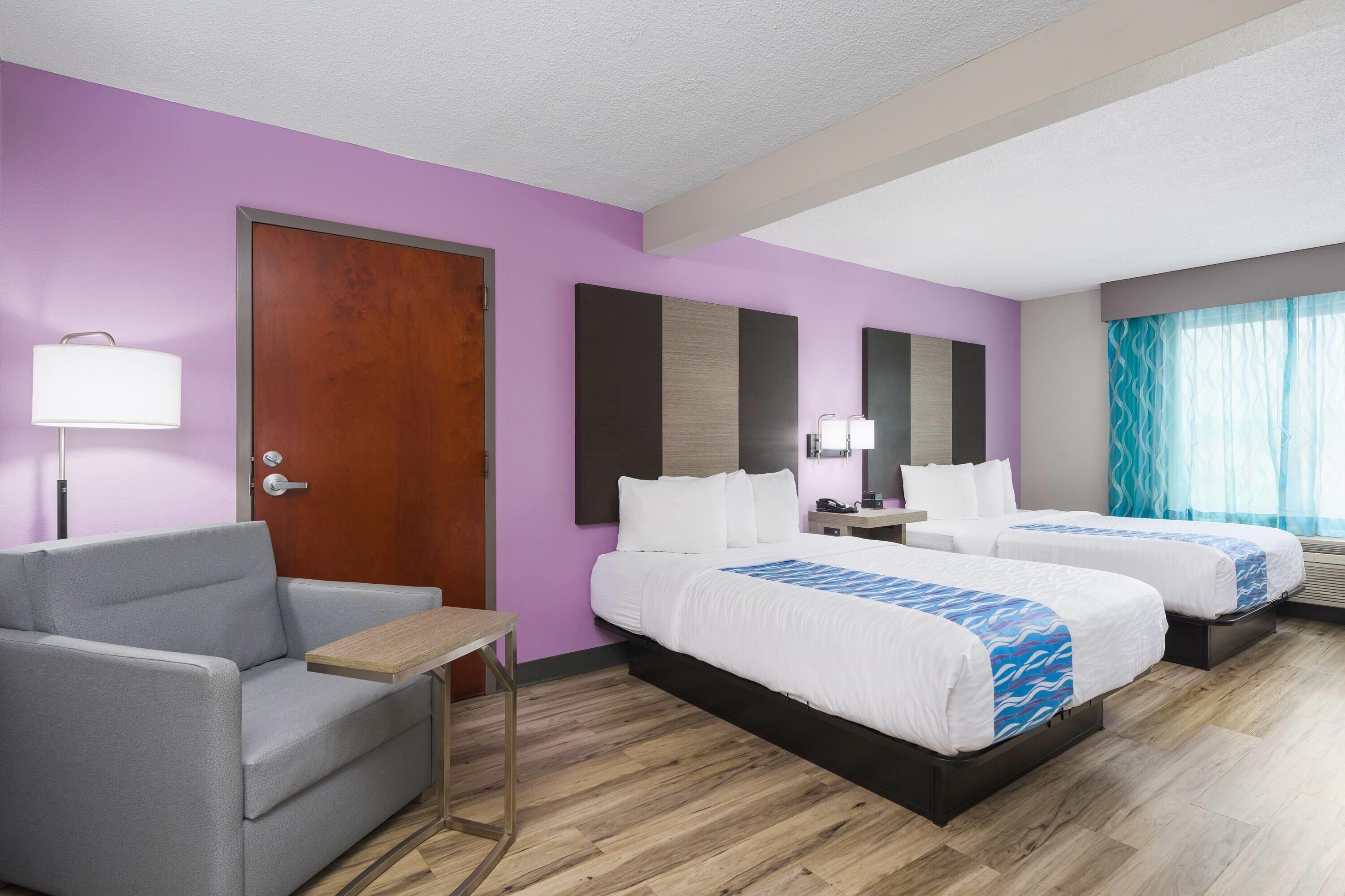 Ein Hotelzimmer mit zwei Betten, einem Schlafsofa, einem Schreibtisch und einem Fenster mit Vorhängen.
