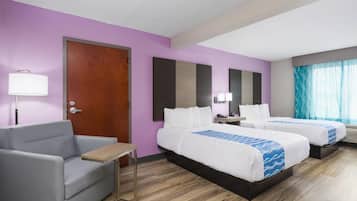 A hotel room with two beds, a sofa, a desk, and a window with curtains.