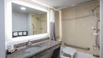 A bathroom with a granite countertop sink, a mirror, a shower with a grab bar, and a white toilet.