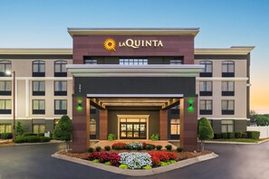 Un hotel La Quinta con una entrada moderna, un emblema de sol y un jardín bien cuidado.