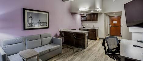 A modern apartment with a grey sofa, a small wooden table, a kitchen area with a microwave, and a TV.