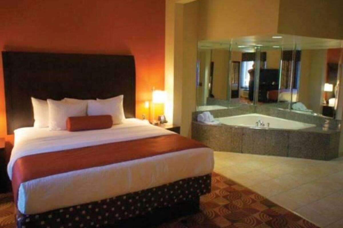 Habitación de hotel con una cama grande, baño independiente con bañera y un espejo que refleja la habitación.