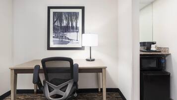 A hotel room with a desk, chair, lamp, and a microwave.