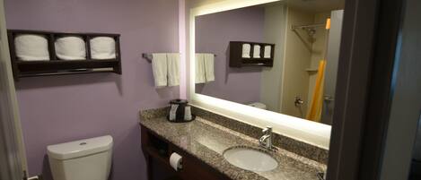A bathroom with a toilet, sink, and mirror. There are towels on the wall and a shelf above the sink.