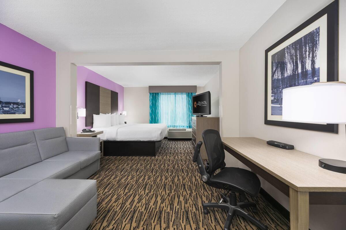 Una habitación de hotel con cama, escritorio, silla, televisor y sofá.