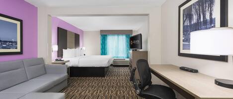 A hotel room with a bed, a desk, a chair, a TV, and a couch.