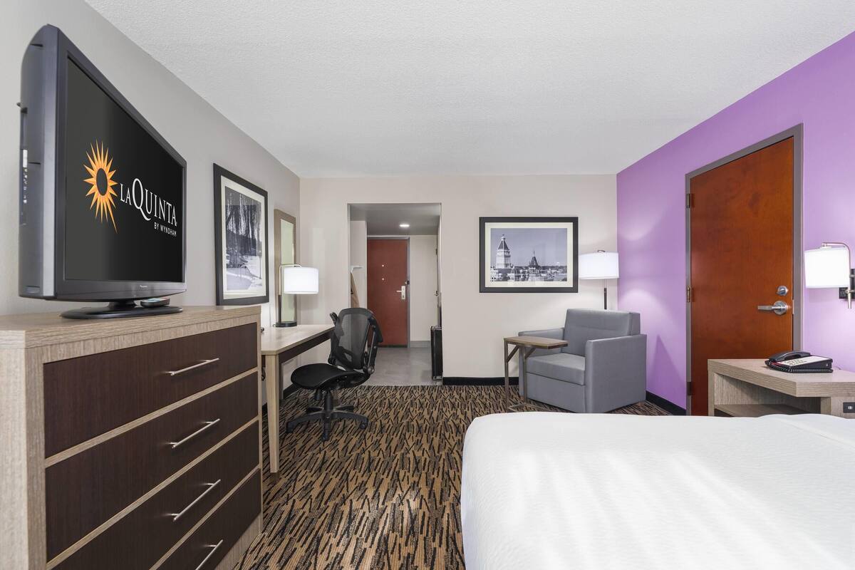Una habitación de hotel con cama, escritorio, silla, televisor y puerta.