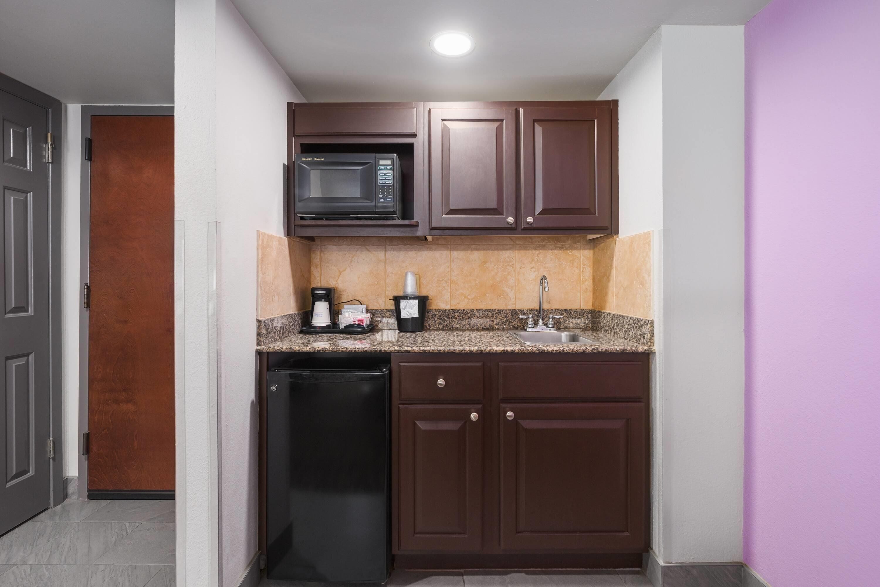 Una cocina compacta con microondas integrado, cafetera y lavamanos.
