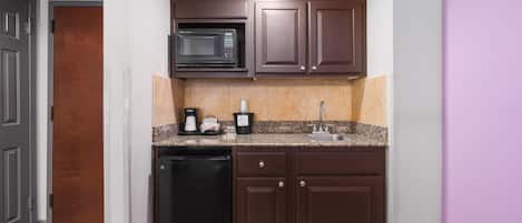 Una cocina compacta con microondas integrado, cafetera y lavamanos.