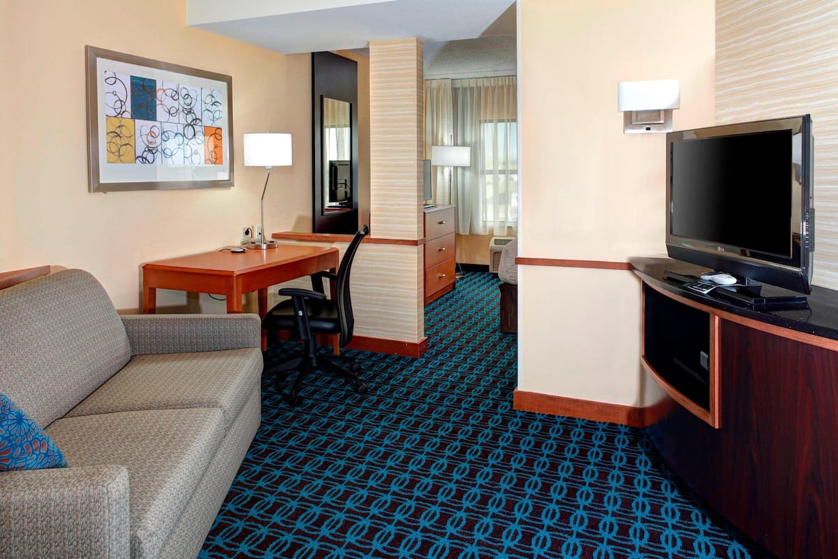 A hotel room with a sofa, a desk with a computer, a TV, a mirror, and a patterned carpet.