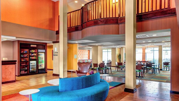 A hotel lobby with a curved blue sofa, a corner market, and a dining area with tables and chairs. - Fairfield by Marriott Inn & Suites Anniston Oxford (Oxford)