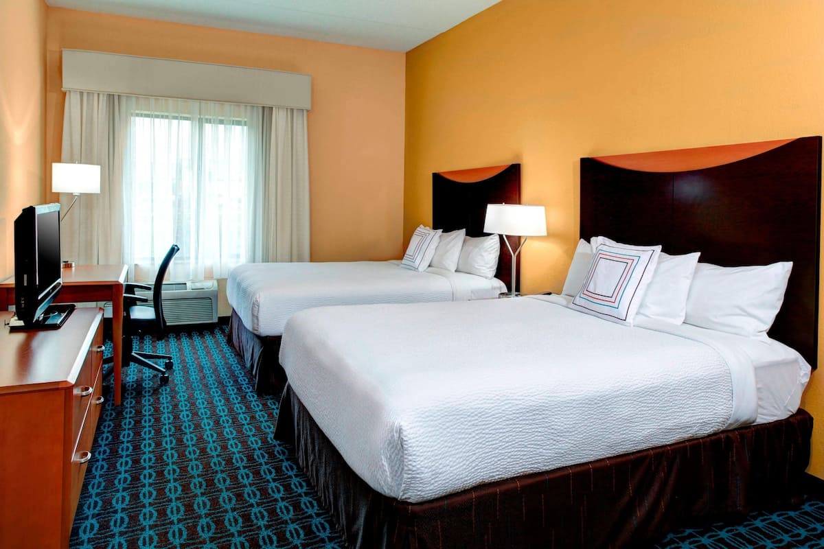 A hotel room with two beds, a desk with a computer, a chair, and a television.