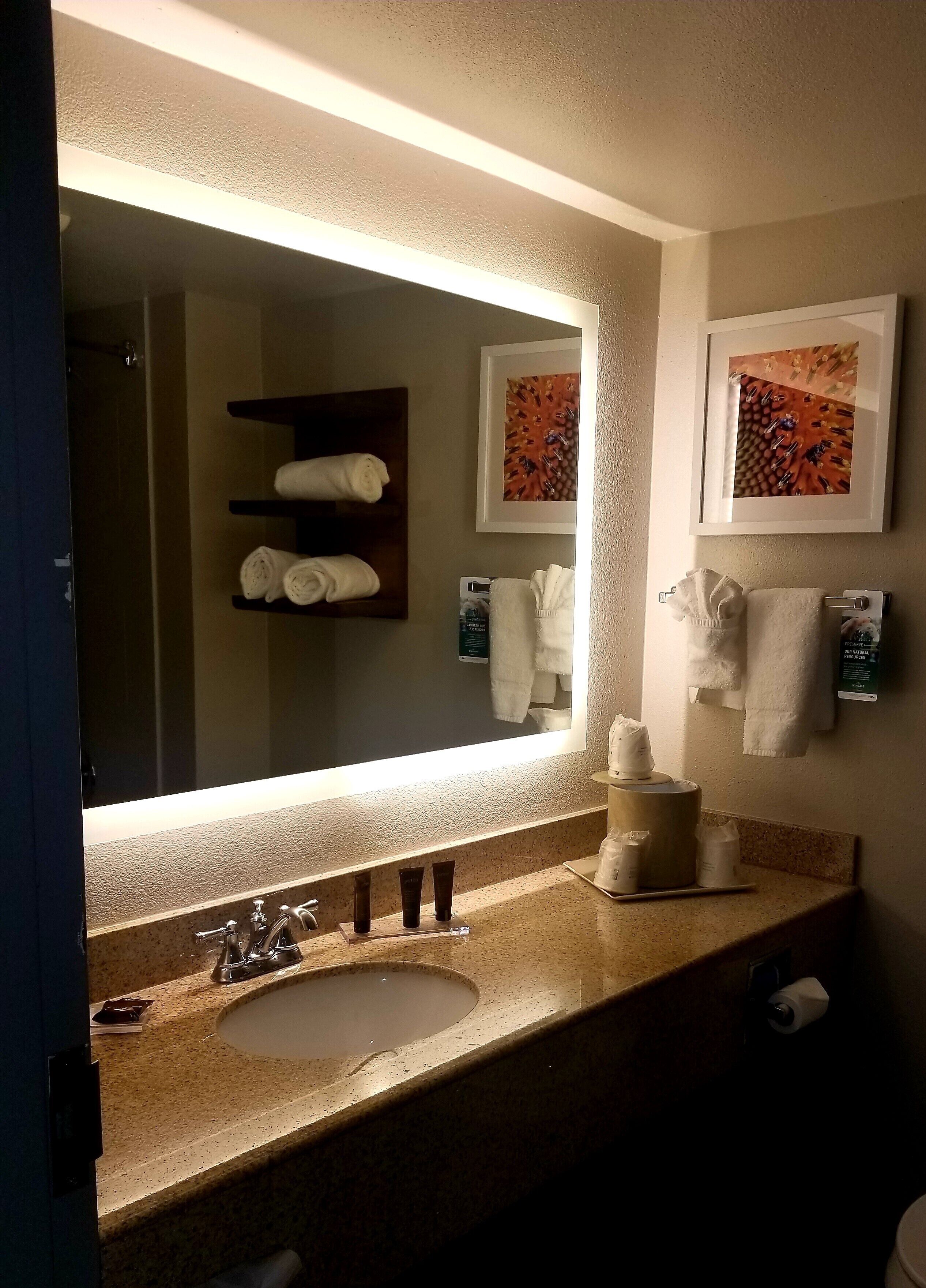 Un baño con un espejo grande, un lavamanos y dos toalleros.