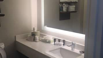 Un baño con lavamanos blanco, un espejo y un estante con toallas y artículos de aseo.