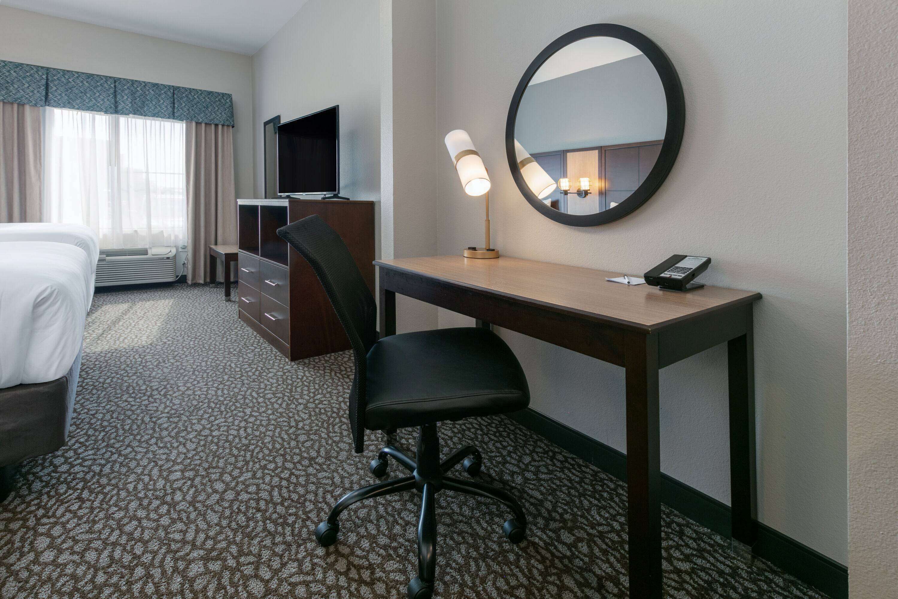 Habitación de hotel con cama, escritorio, silla, lámpara de escritorio, teléfono y un espejo grande.