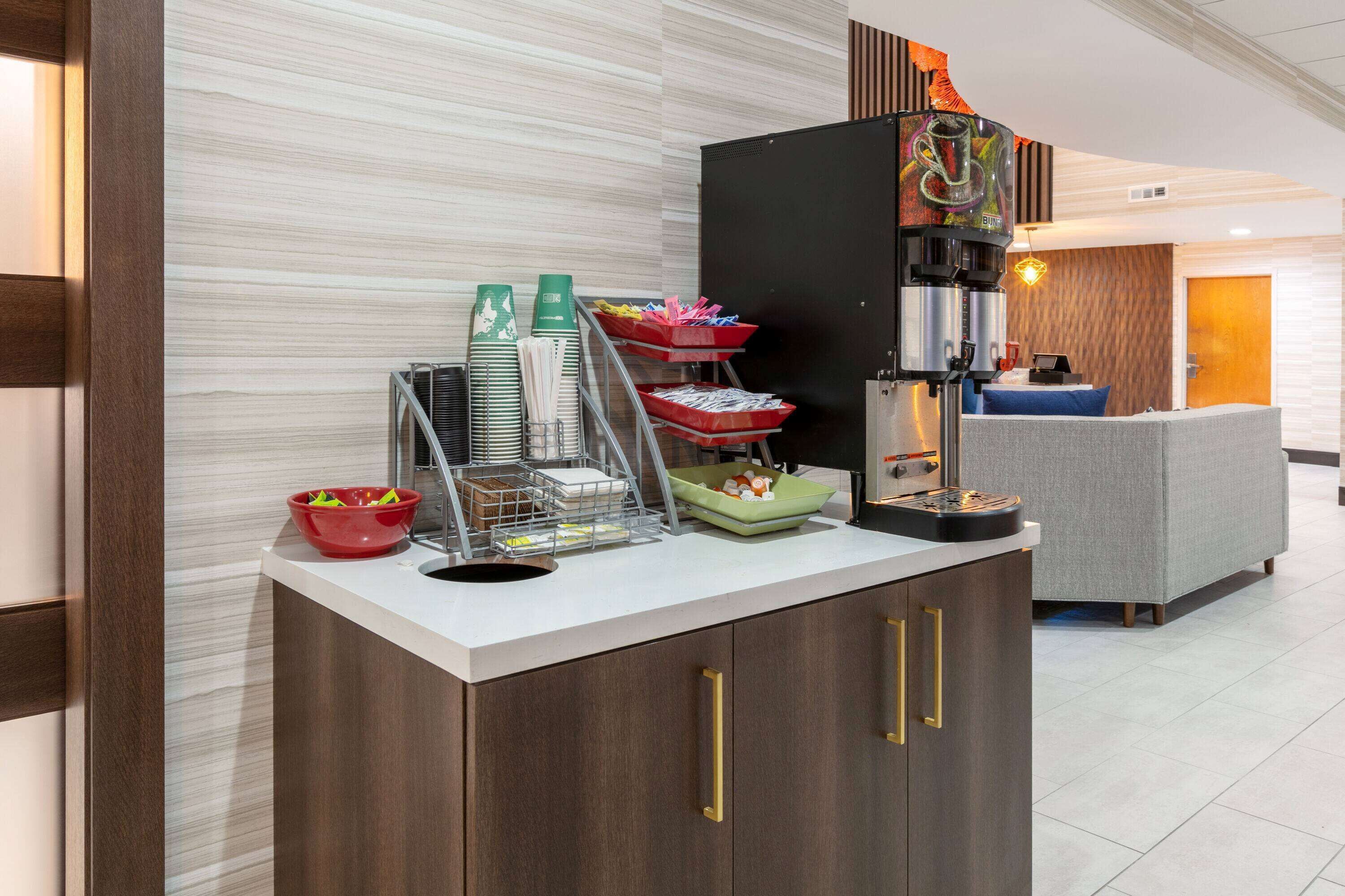 Zona cuina moderna amb cafetera, plats apilats, bols i nevera.