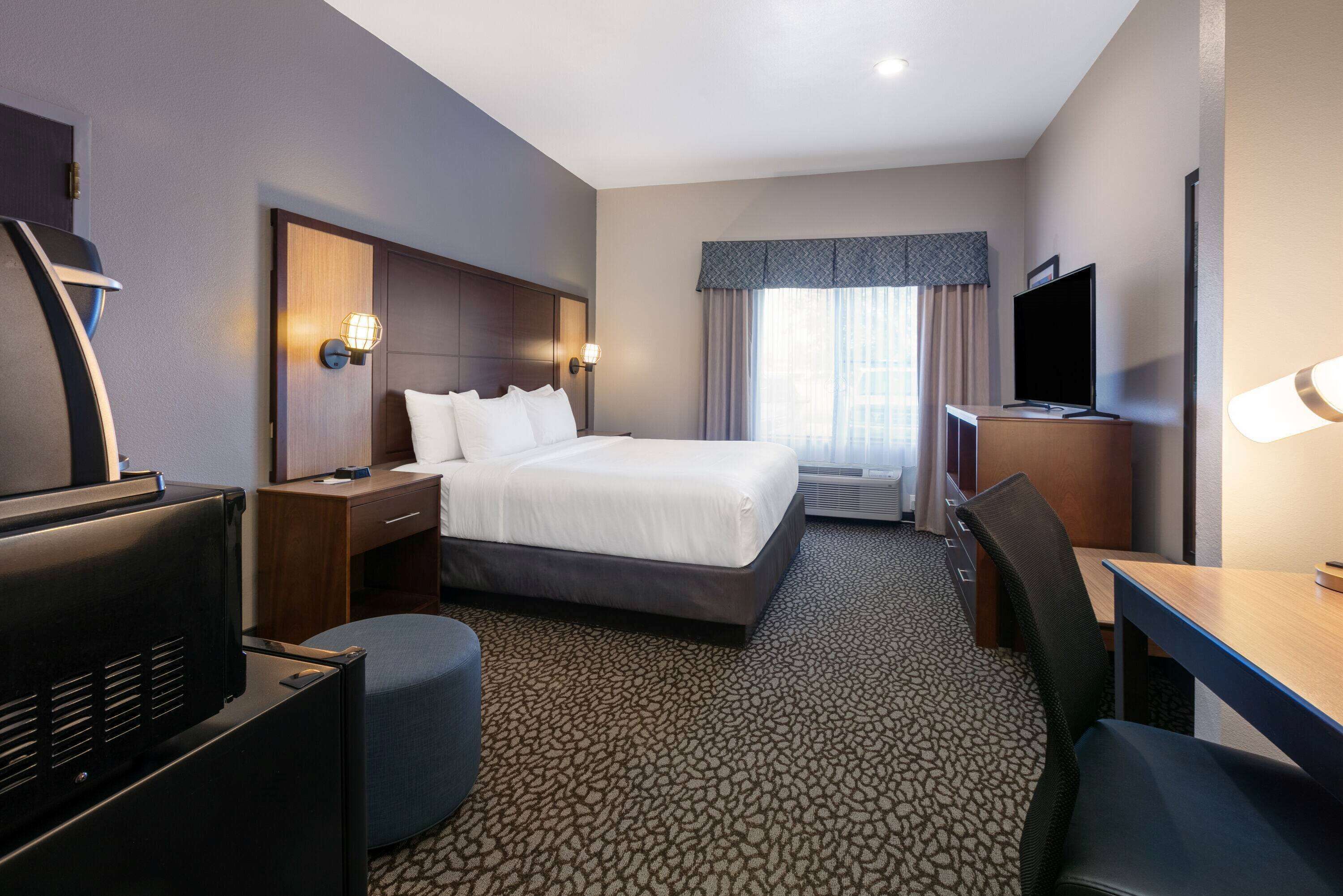 Una habitación de hotel con una cama, un escritorio, un televisor y una silla.