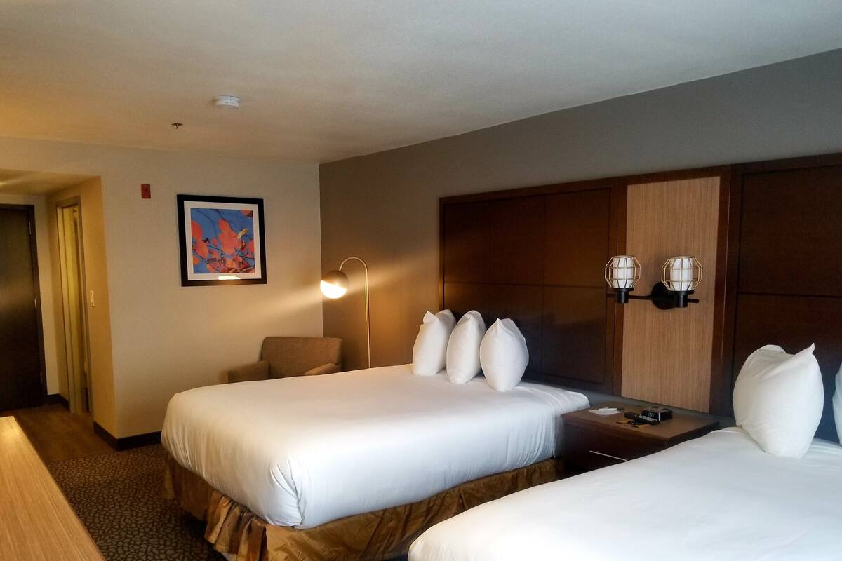 Ein Hotelzimmer mit zwei Betten, einem hölzernen Kopfteil, einem Nachttisch mit Lampe und einem gerahmten Bild an der Wand.