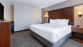 Una habitación de hotel con una cama grande, un cabecero de madera, una mesita de noche y una lámpara fijada a la pared.