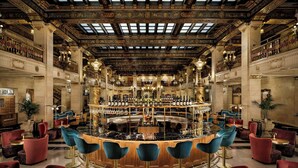 A grand bar area with a central bar, multiple seating options including bar stools and cushioned chairs, and a high ceiling with intricate designs. - The Louie, A Davenport Hotel, Autograph Collection® (Spokane)