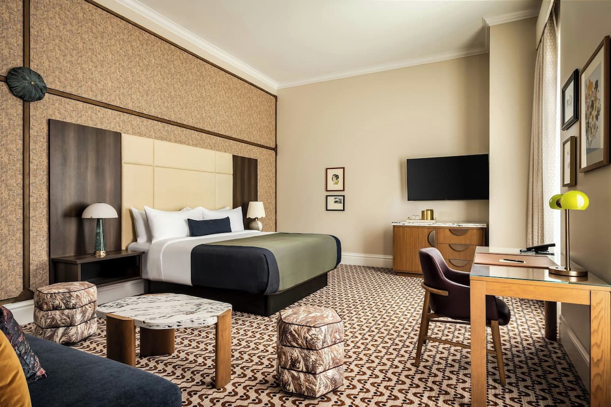 Ein Hotelzimmer mit Bett, Schreibtisch, Stuhl, Fernseher und einem gemusterten Teppich.