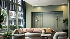 A modern interior with a sofa, ottomans, and a view of a building with flags. - The Louie, A Davenport Hotel, Autograph Collection® (Spokane)