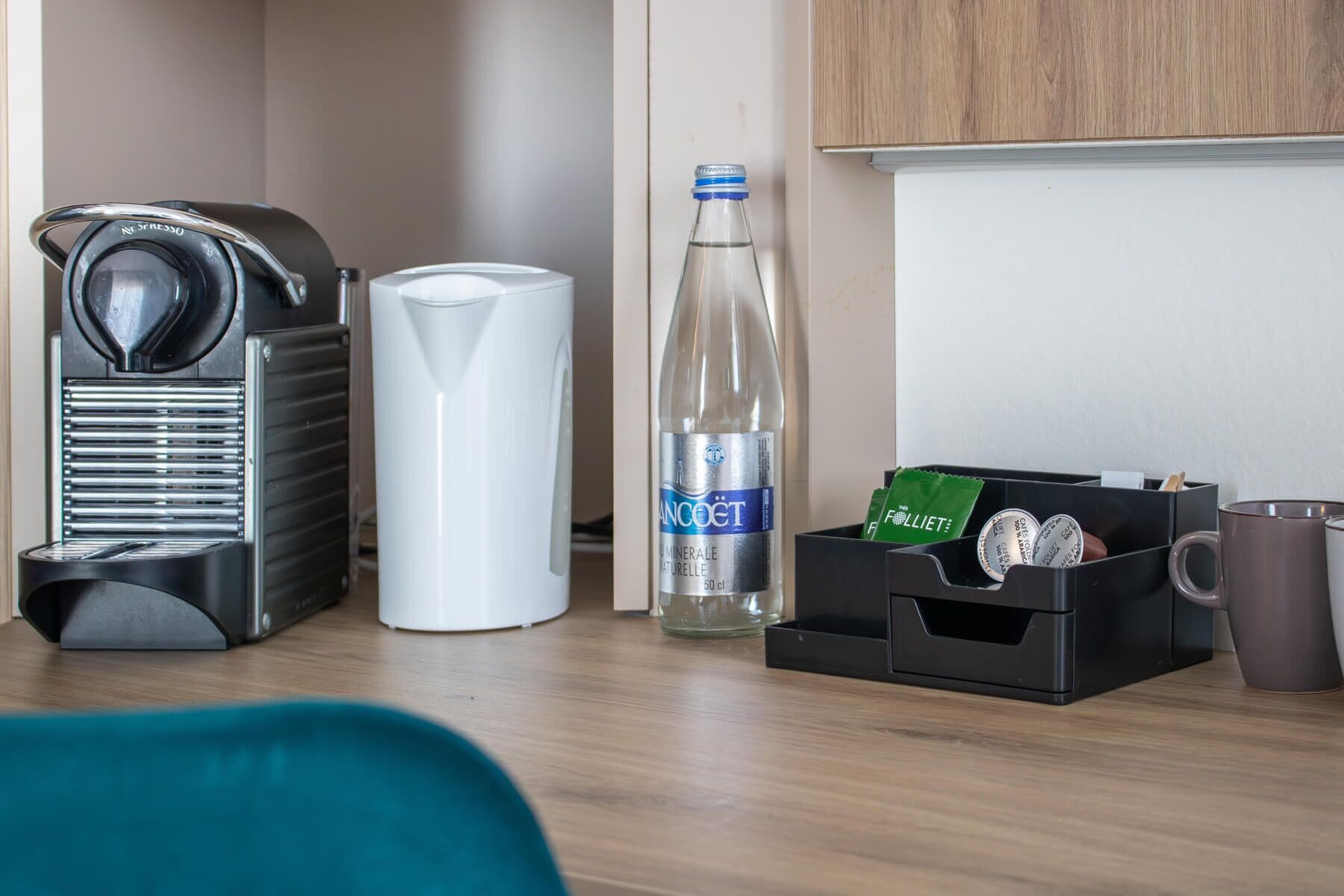 Una kitchenette con cafetera, una botella de agua, una taza y una caja de bolsitas de té.