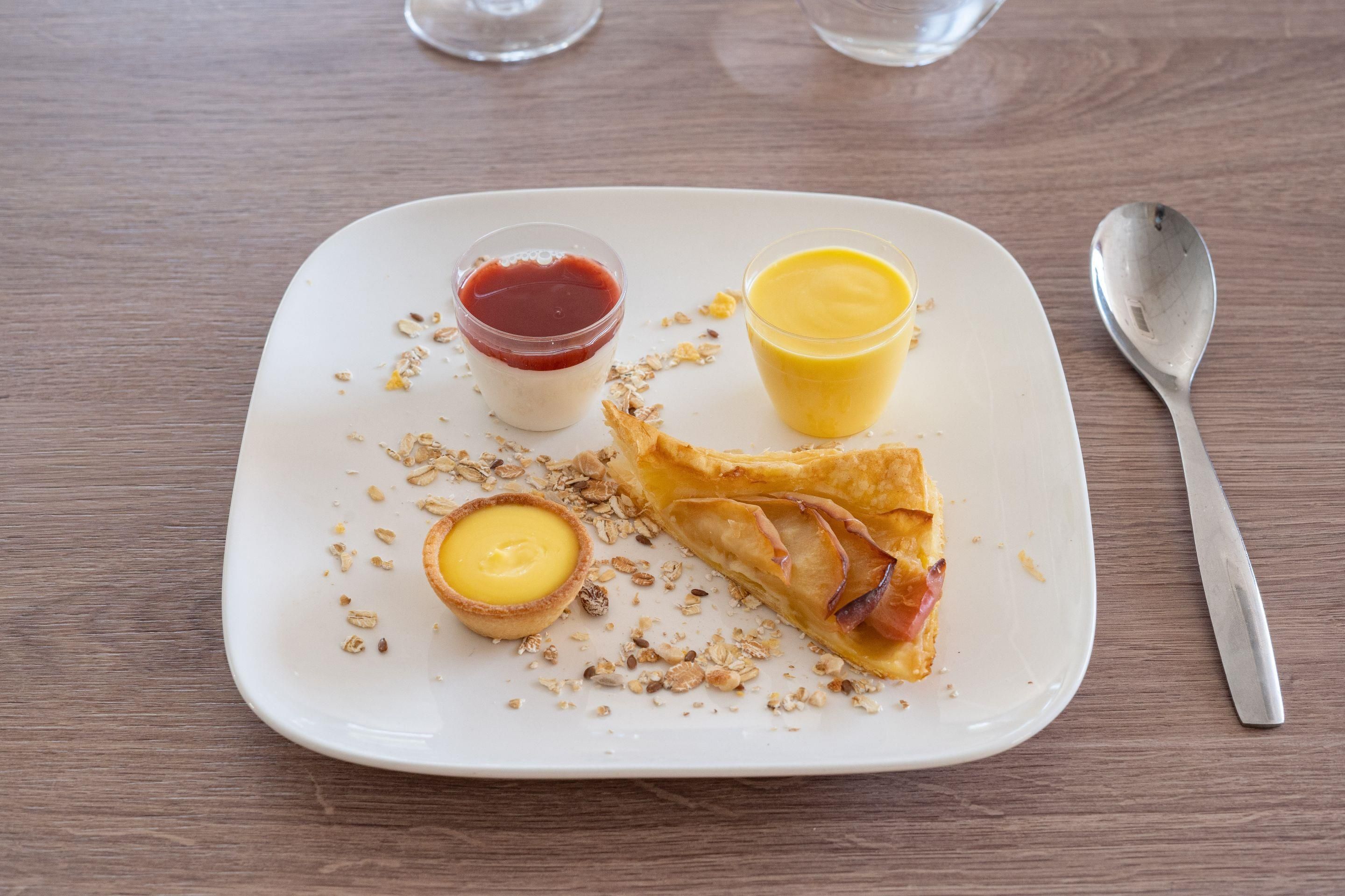 Une assiette contenant divers aliments, notamment une tarte, un verre de jus d’orange et un petit pot de confiture.