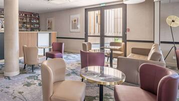 A hotel lobby with seating areas, a bar with a variety of bottles, and a large window providing natural light.