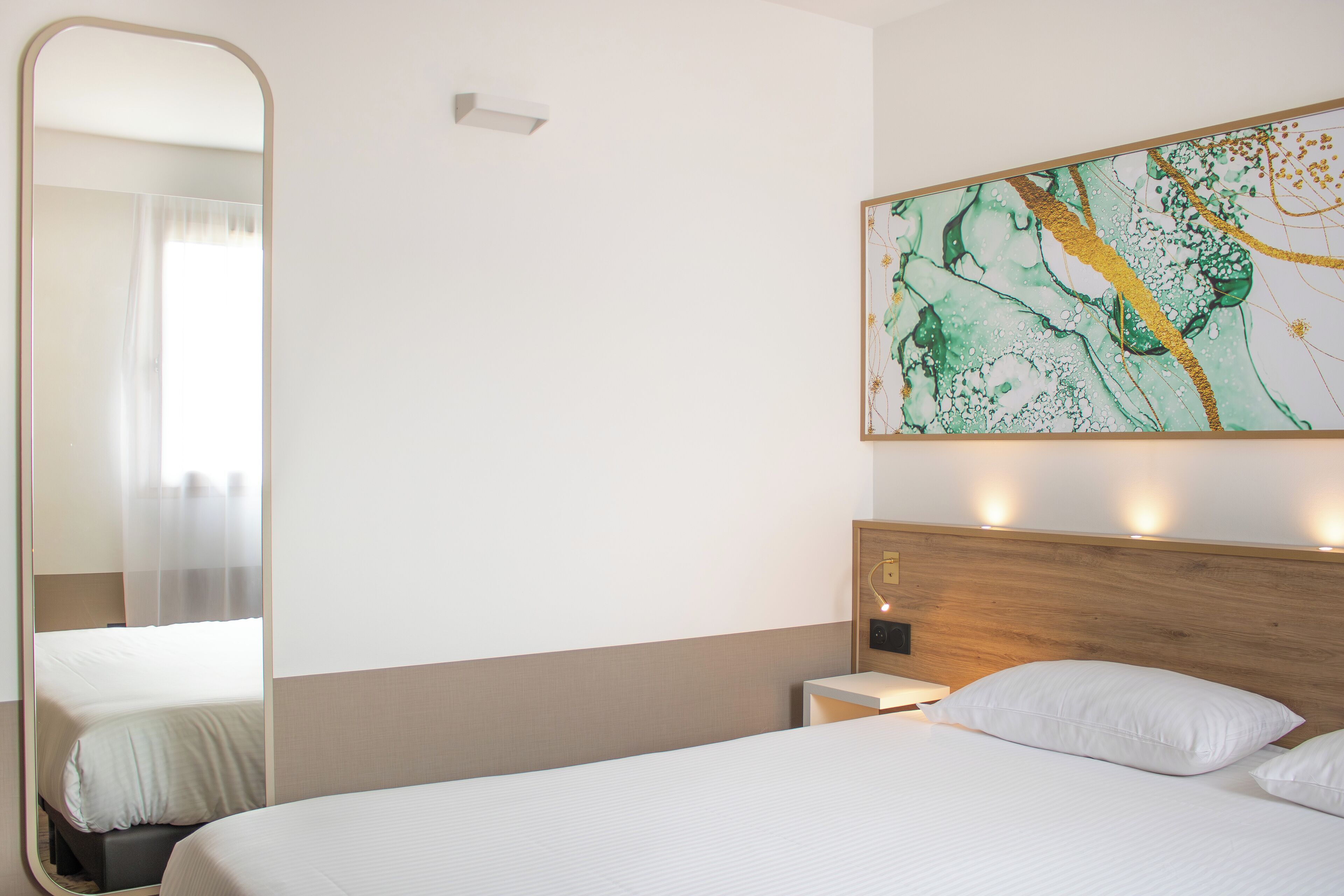 A hotel room with a large bed, a nightstand, a wall-mounted light, and a large abstract painting.