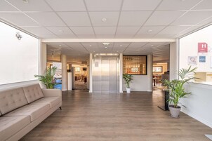 Um saguão de hotel com piso de madeira, um sofá bege, plantas em vasos e um balcão de recepção.