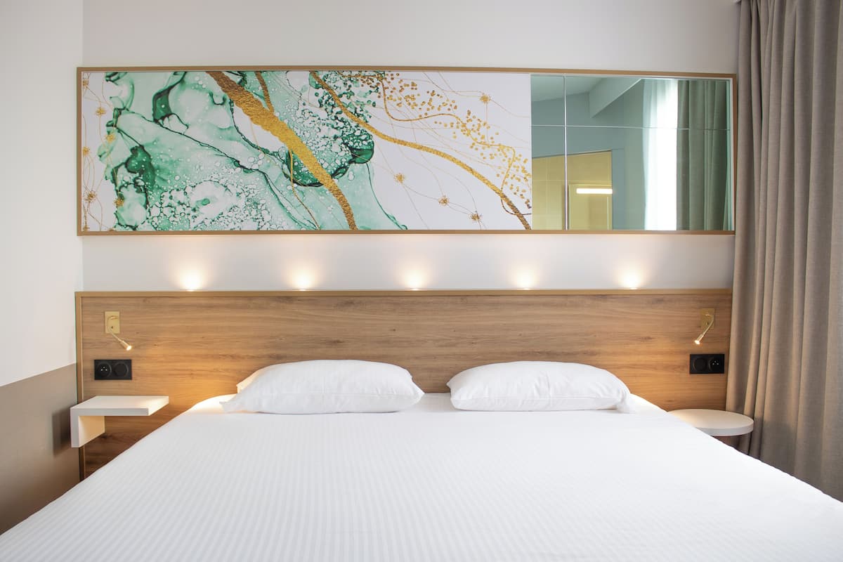 Een hotelkamer met een groot bed, een houten hoofdbord, nachtkastjes, een spiegel aan de muur en een groot abstract schilderij.