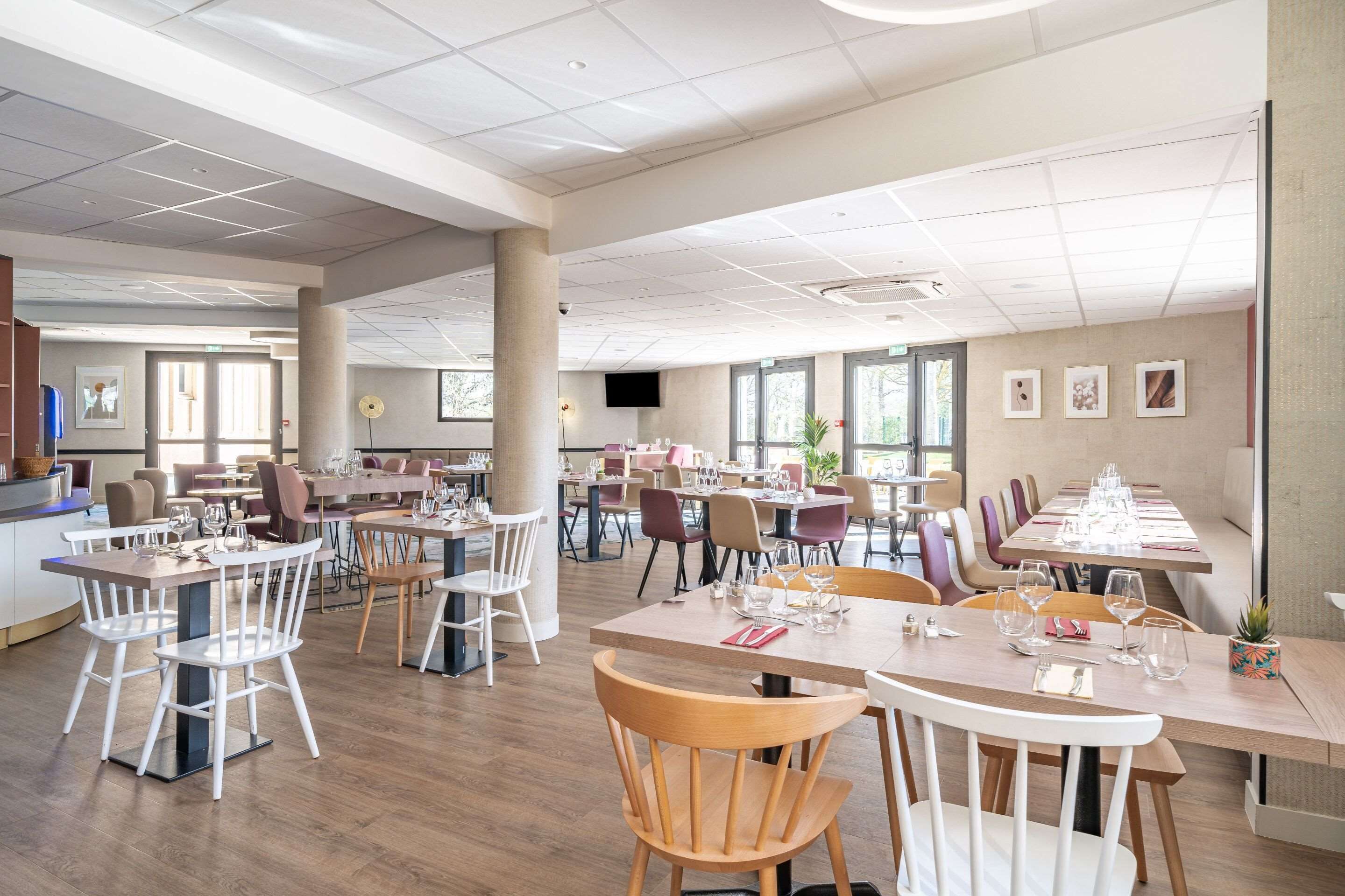 Een ruime eetruimte met meerdere tafels en stoelen, grote ramen en een modern plafondontwerp.