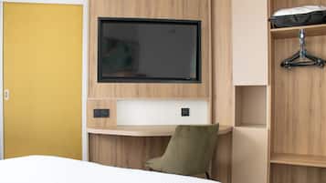 A hotel room with a bed, a TV mounted on the wall, a wooden desk, and a wardrobe.