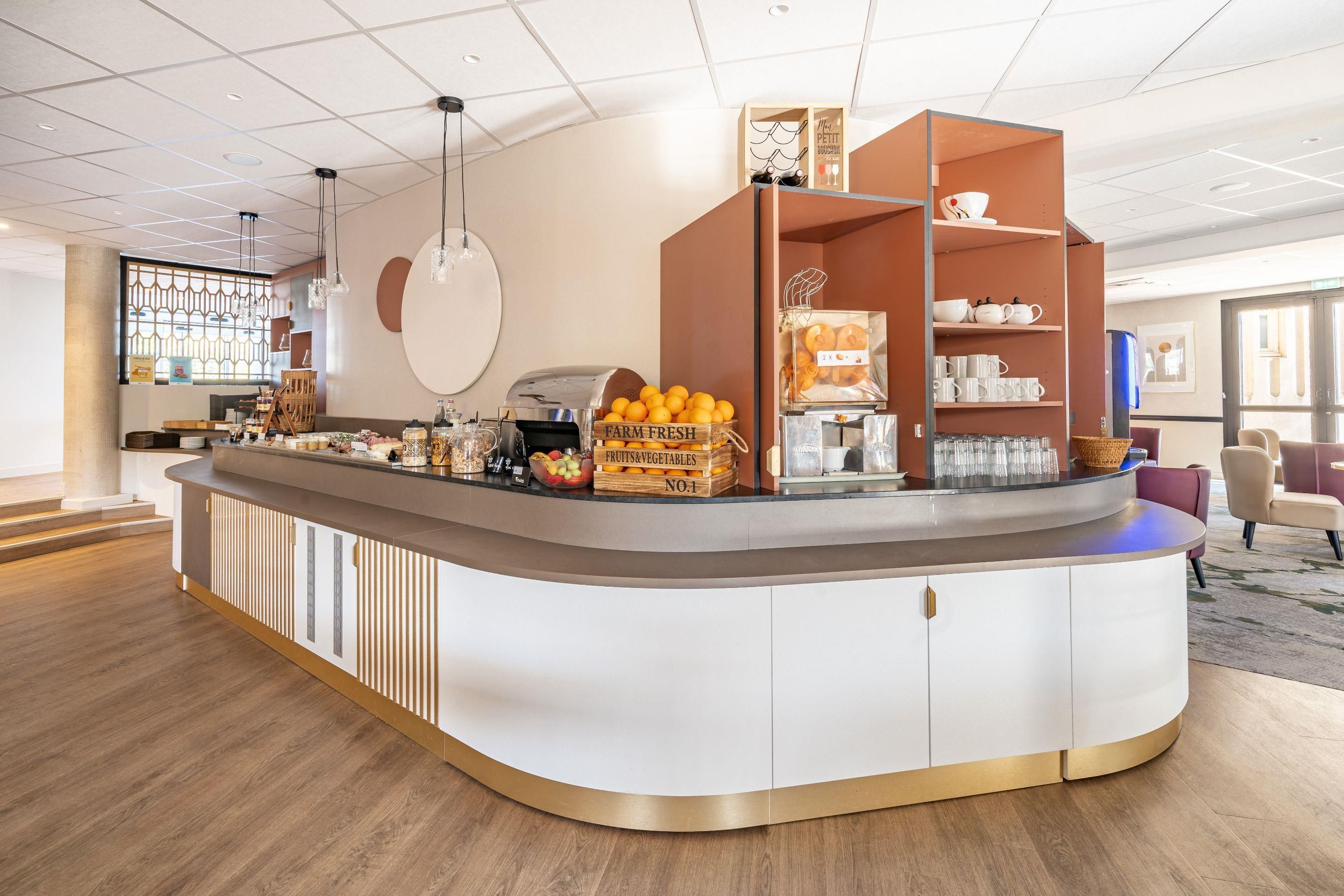 Un hall d'hôtel moderne avec un comptoir central, un présentoir de fruits et un espace salon.