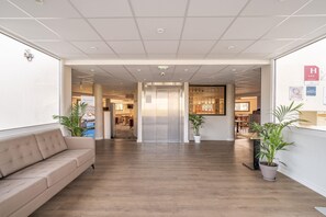 Un hall d’hôtel avec un comptoir d’accueil, un canapé et des plantes en pot.