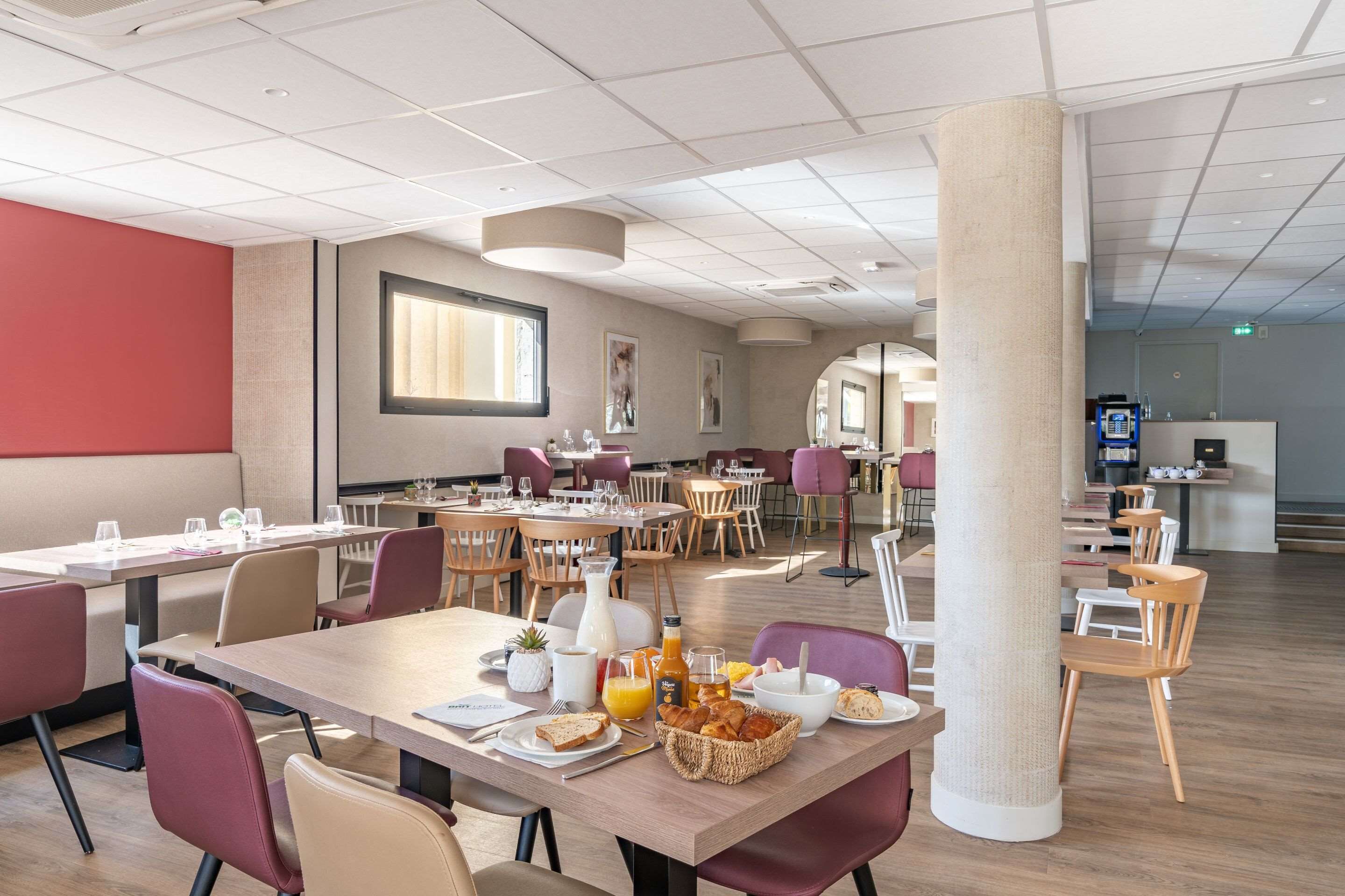 A modern dining area with multiple tables and chairs, a large pillar, and a reception desk in the background.