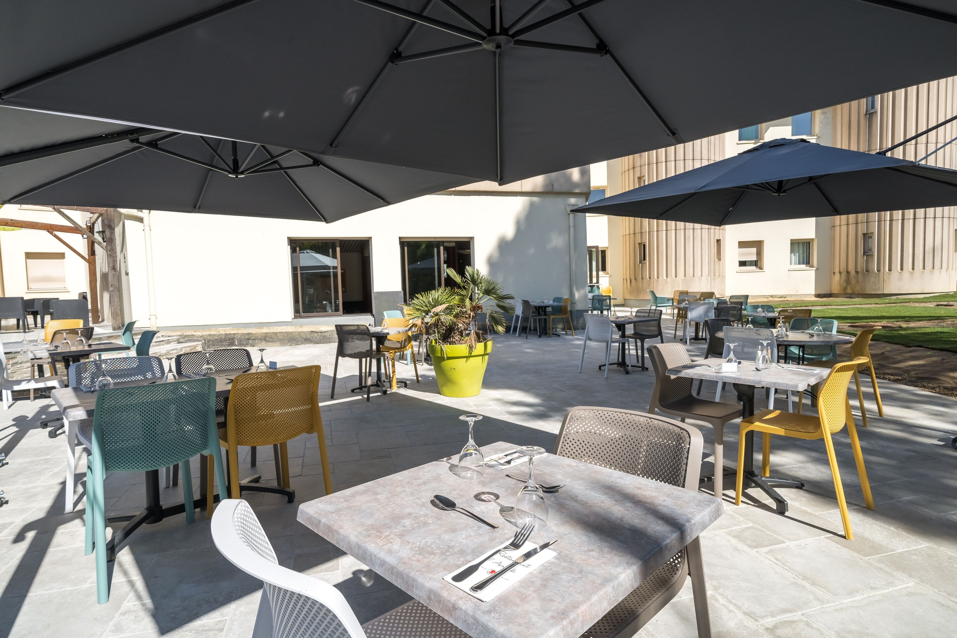 An outdoor patio area with tables and chairs, umbrellas, and potted plants.