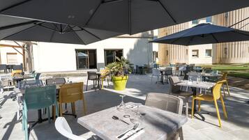 An outdoor patio area with tables and chairs, umbrellas, and potted plants.