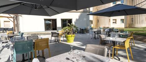 Un patio al aire libre con mesas, sillas, sombrillas y plantas en macetas.