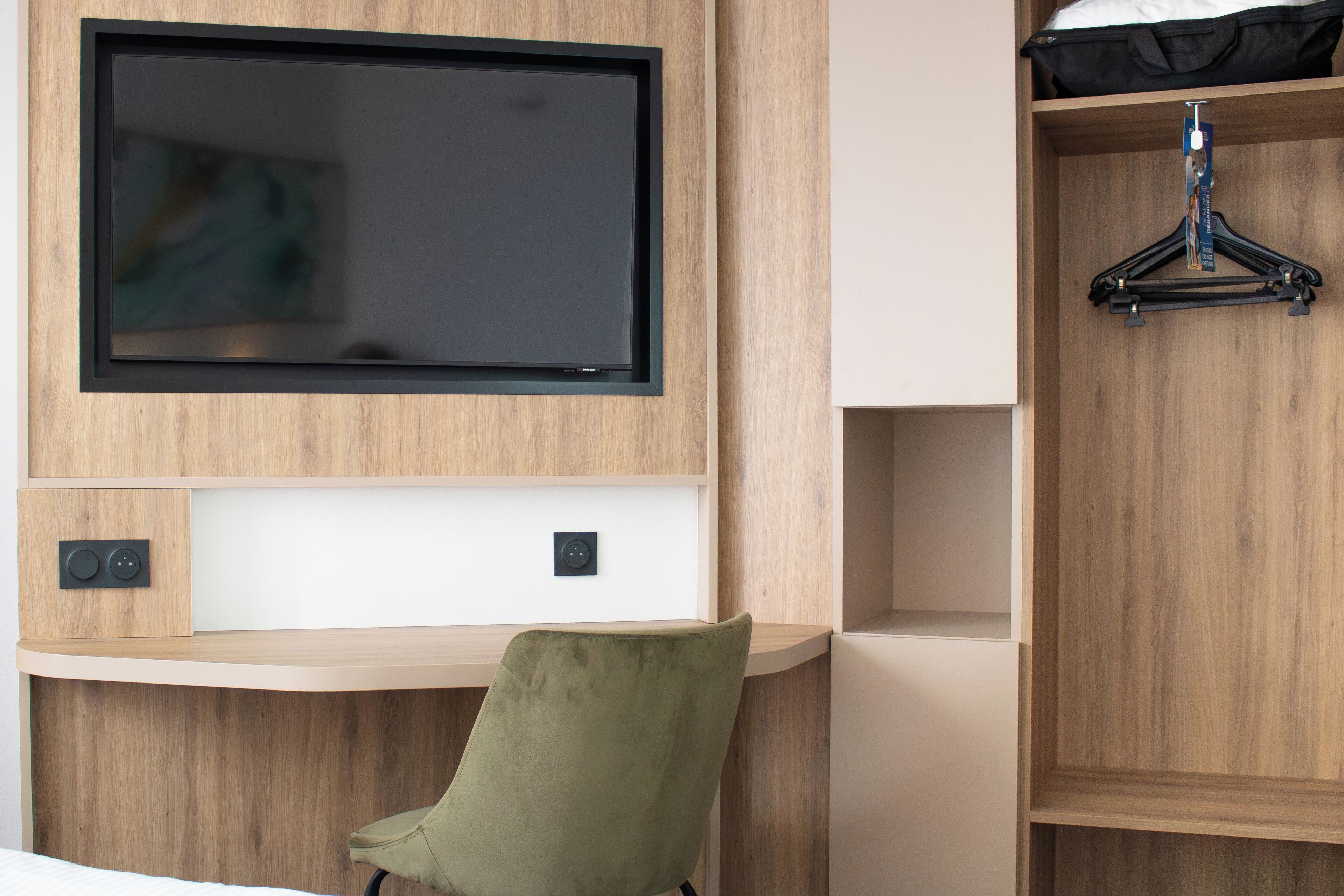 Ein modernes Zimmer mit montiertem Fernseher, einem Schreibtisch und einem an der Wand befestigten Kleiderhaken.