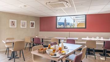 A dining area with tables and chairs, breakfast items, and framed pictures on the wall.