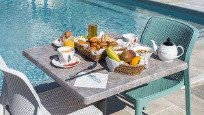 Un buffet de petit-déjeuner installé au bord de la piscine, avec des croissants, des fruits et une théière portant l’inscription « FILIET » sur une table.