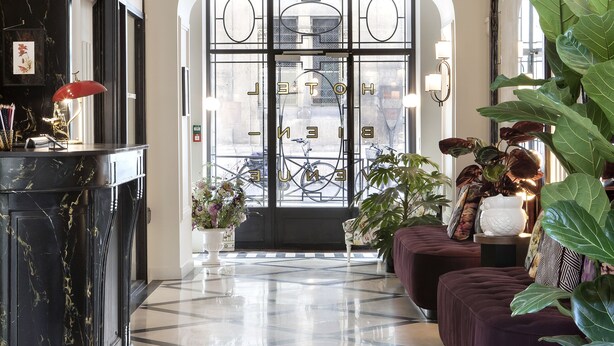 A spacious lobby with a checkered floor, a reception desk, seating area, and large windows with a view of the city. - Hotel Bienvenue (Paris)