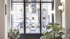 A hotel entrance with a glass door, a potted plant, a purple sofa, and a tiled floor. - Hotel Bienvenue (Paris)