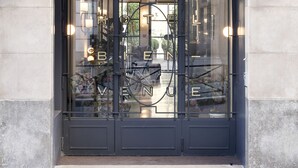 A hotel entrance with a black metal gate, glass doors, and two wall-mounted lights. - Hotel Bienvenue (Paris)