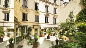 A courtyard with potted plants, outdoor seating, and a building facade with multiple windows and balconies. - Hotel Bienvenue (Paris)